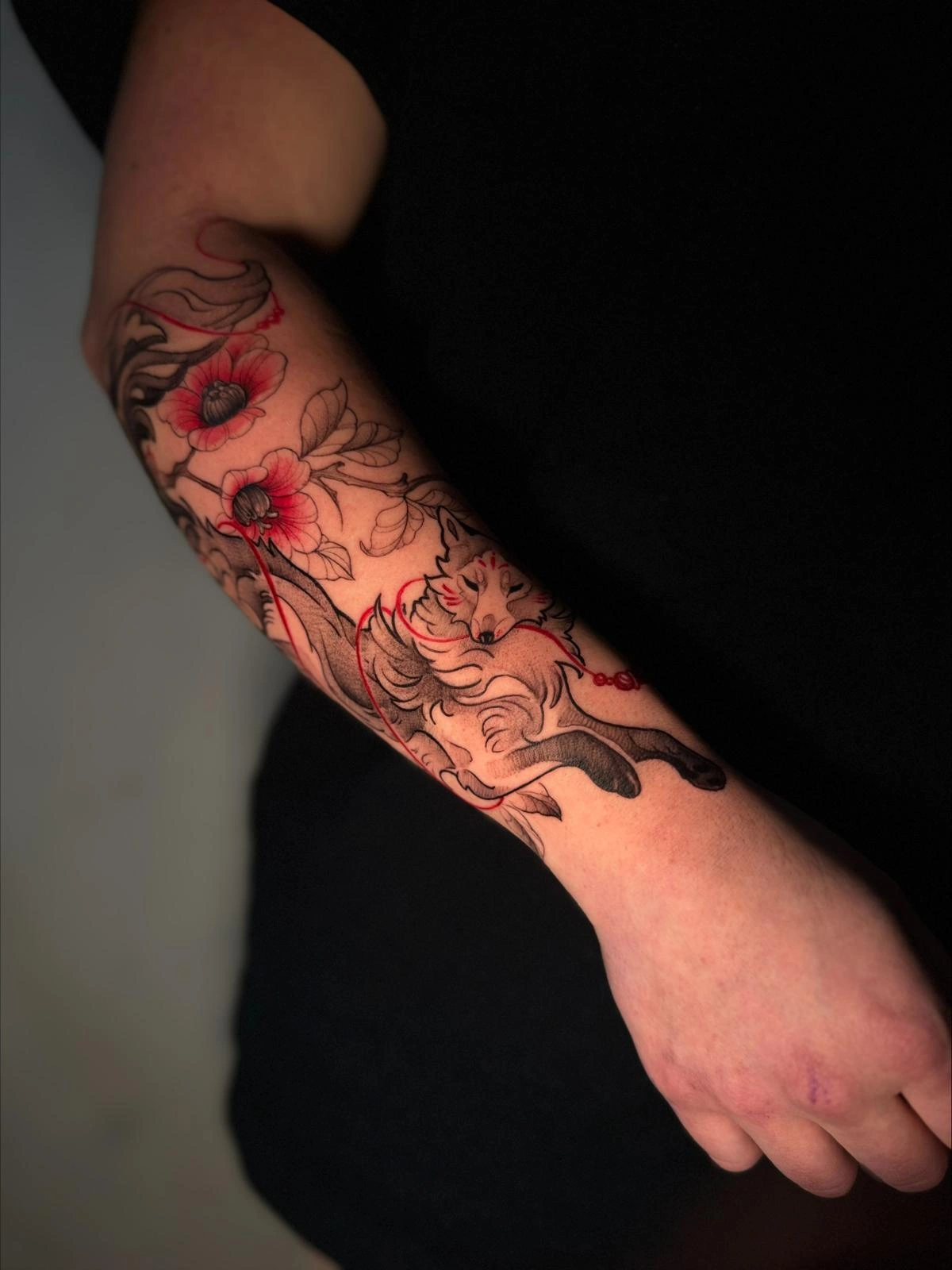 Rote Blüten und schwarze Sketch-Linien als Tattoo auf einem Unterarm