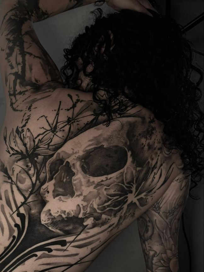 Detail eines schwarzgrauen Schädel-Tattoos mit freien Linien auf dem oberen Rücken